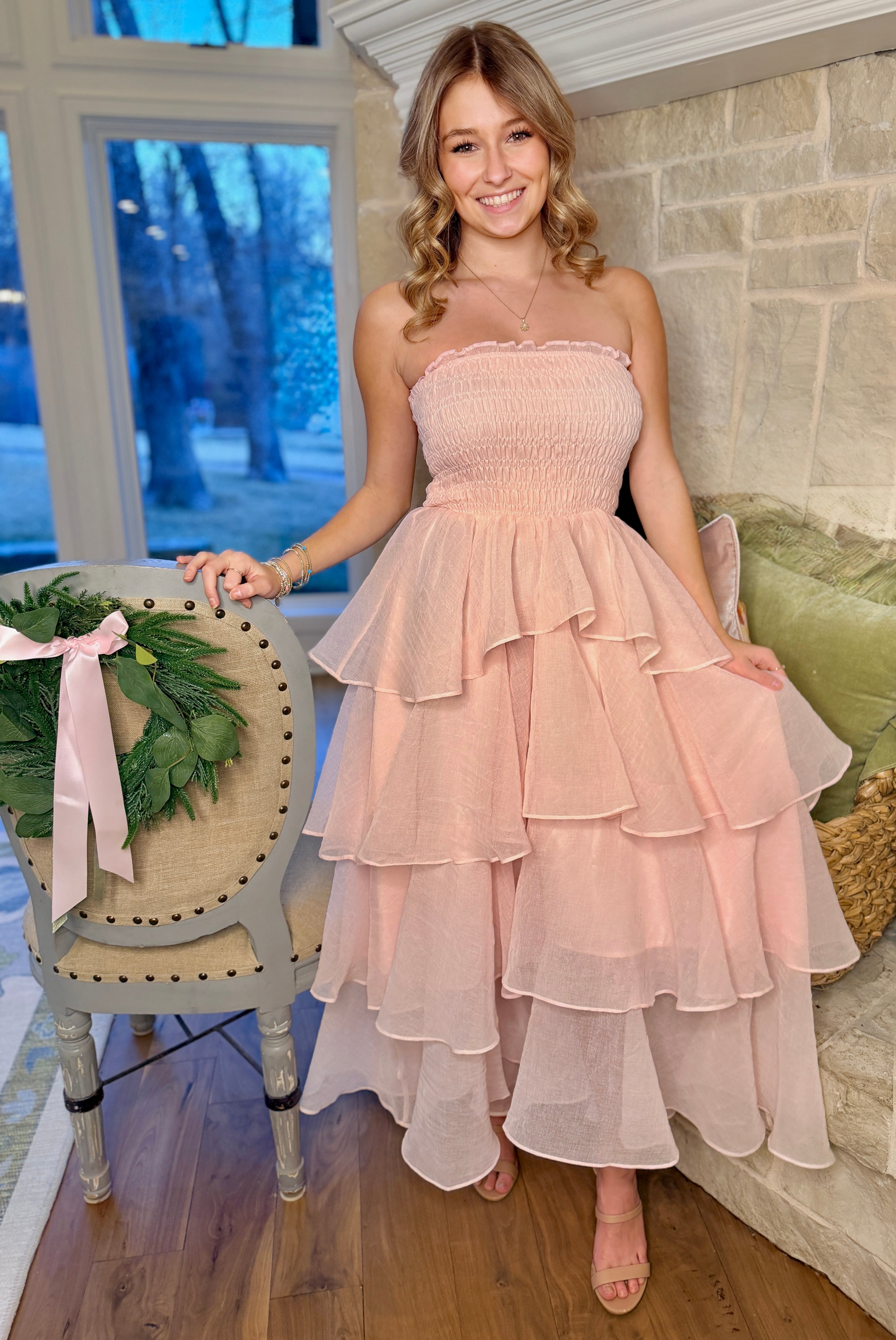 Woman in a pink strapless dress standing in a room with a decorative chair and wreath.