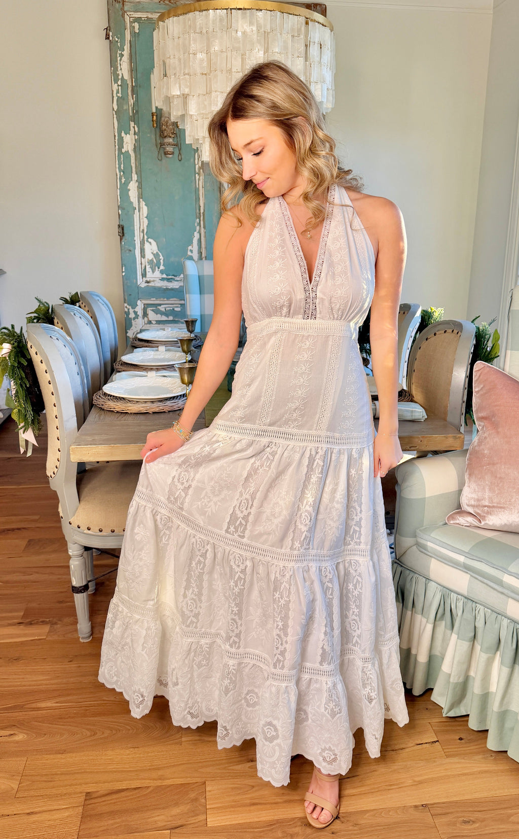 Woman in a white lace dress standing in a room with wooden floor and decorative elements.