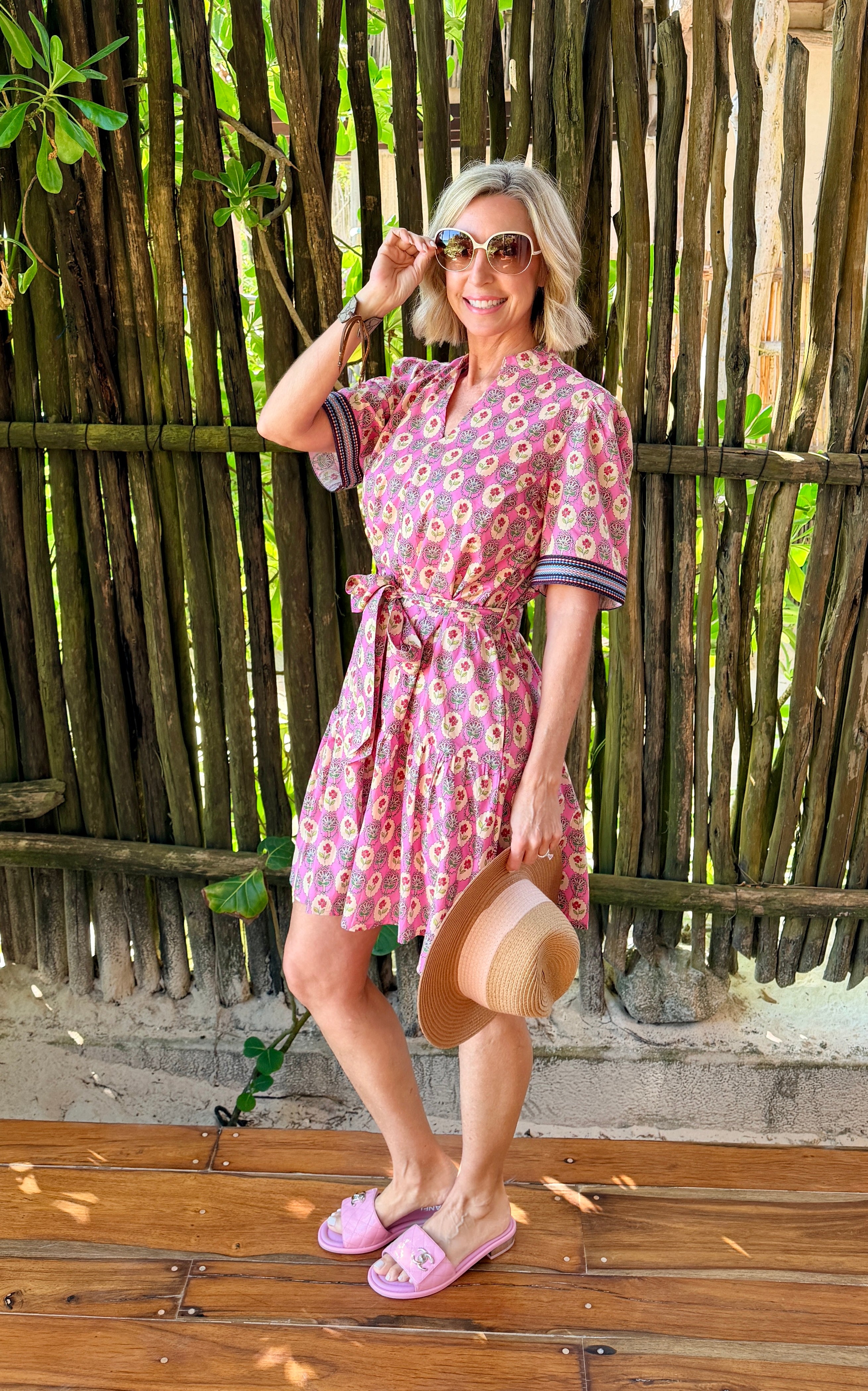 Woman in a pink floral dress standing in front of a wooden fence